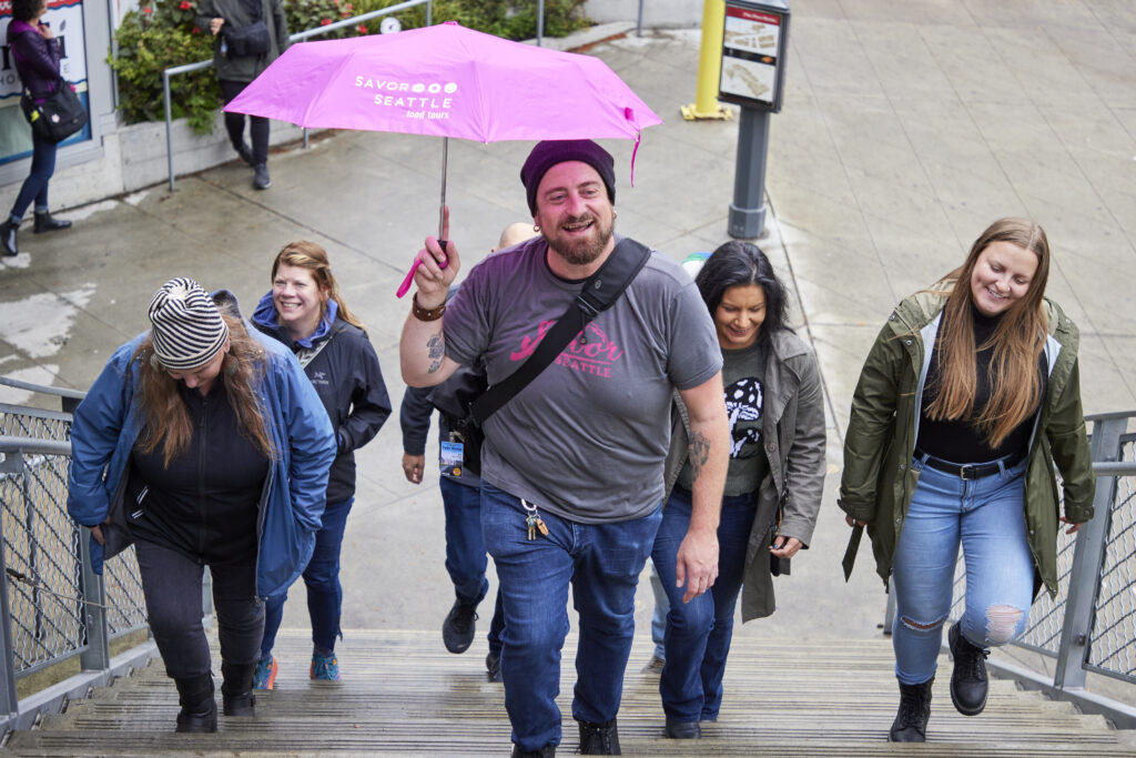 Tour guide Matt Bentley holds the Savor Seattle Tours pink umbrella while conducting a pike place market food tour