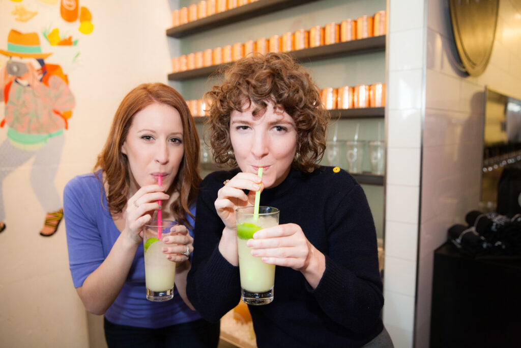 Two women sip fruity drinks through straws during a pike place market food tour.