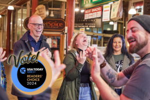 People on Savor Seattle's food tour of Pike Place Market laugh at a joke from the tour guide. Includes a logo that says that Savor Seattle is one of the top food tours in the country